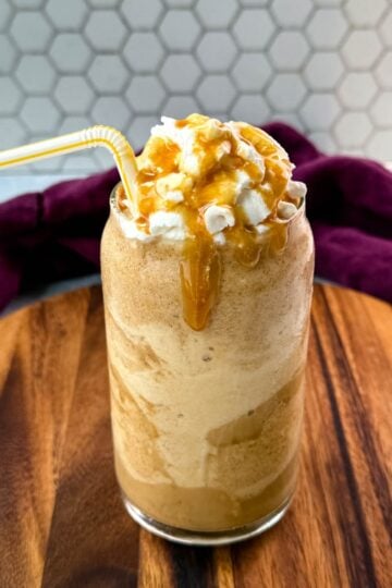 A tall glass of frappe topped with whipped cream and caramel drizzle, served with a straw.
