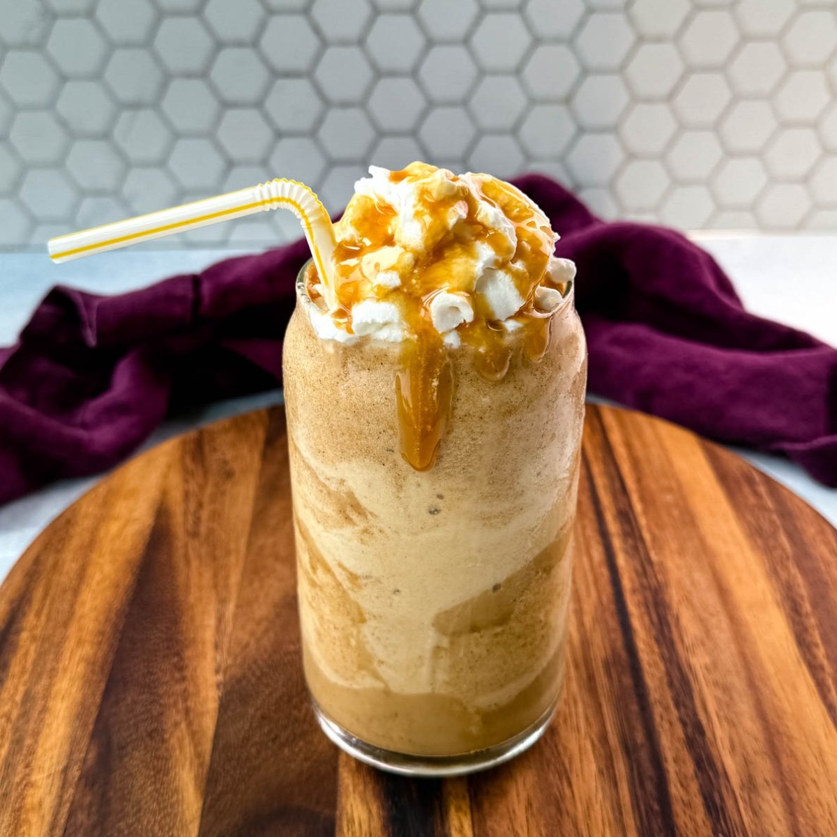 A tall glass of frappe topped with whipped cream and caramel drizzle, served with a straw.