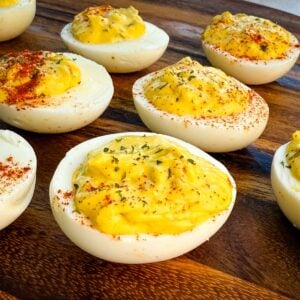 Close-up of Southern-style deviled eggs on a wooden board, topped with paprika and parsley.