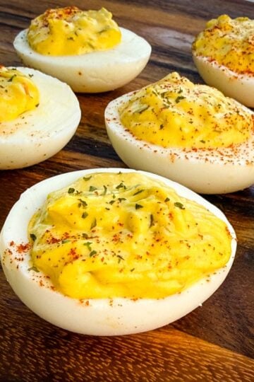 Close-up of Southern-style deviled eggs on a wooden board, topped with paprika and parsley.