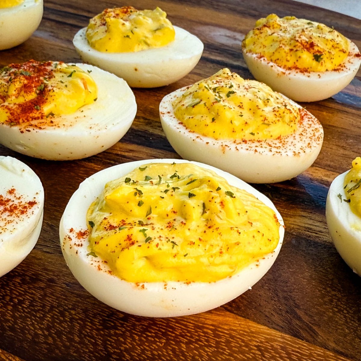 Close-up of Southern-style deviled eggs on a wooden board, topped with paprika and parsley.