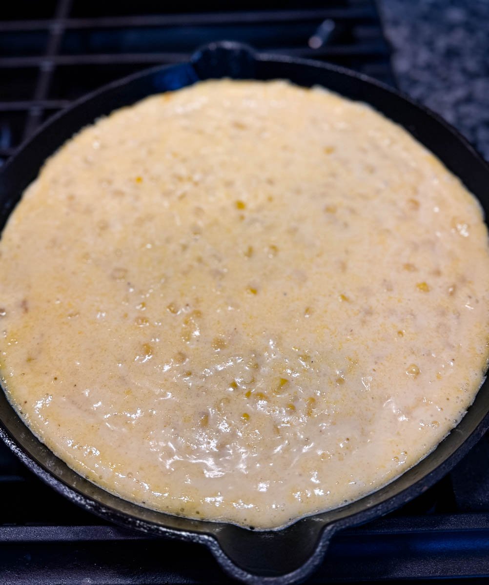 Unbaked Jiffy corn casserole batter in a black cast iron skillet, ready to be baked.