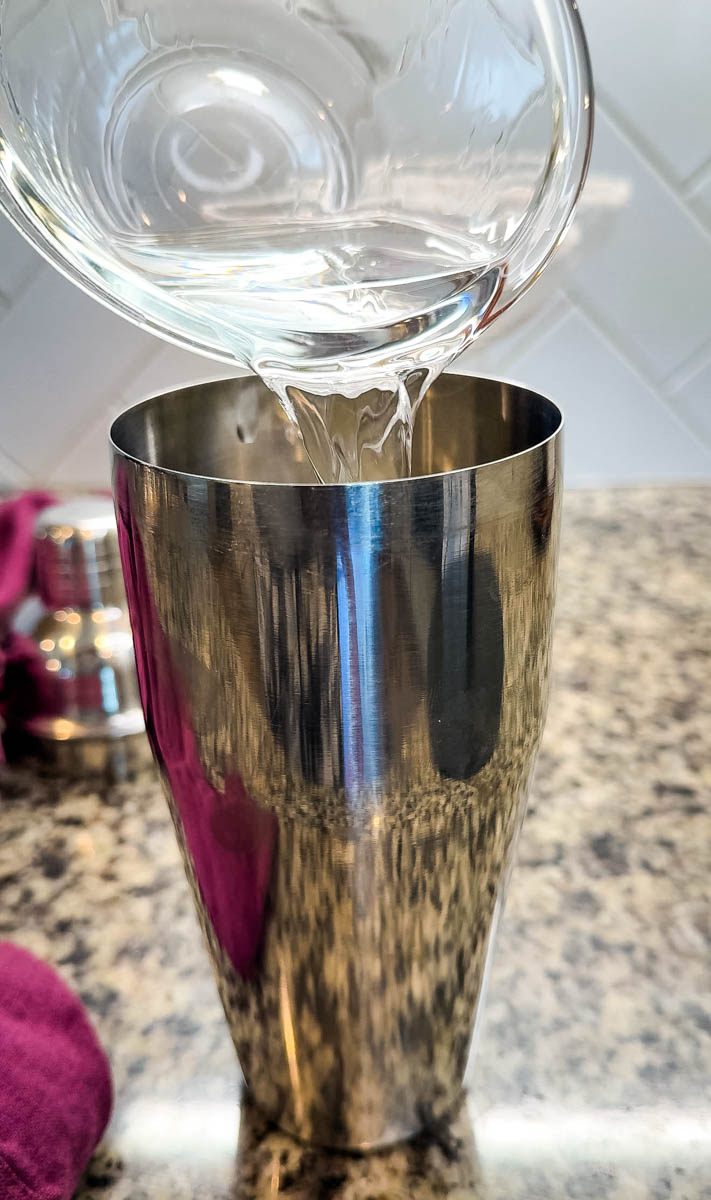 Close-up of vodka being poured into a stainless steel cocktail shaker.