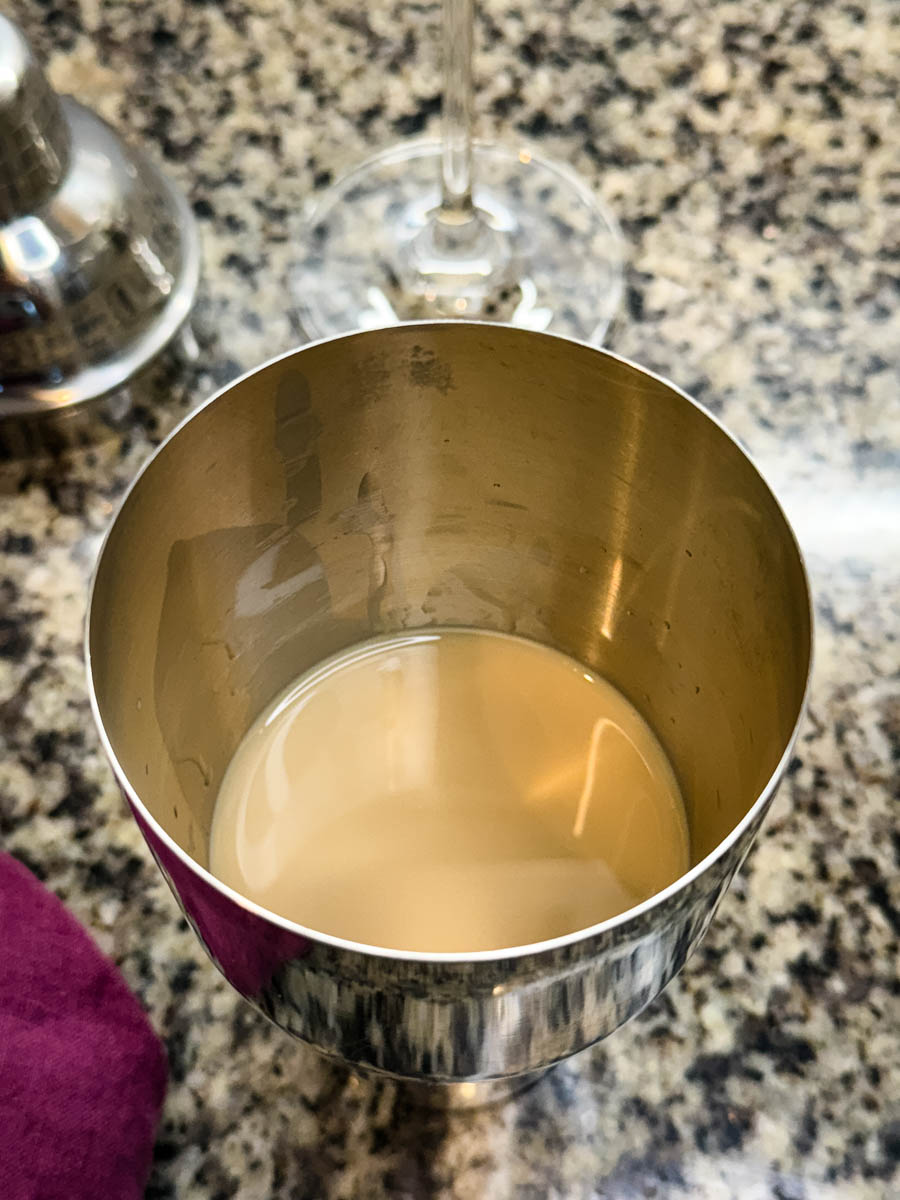 A cocktail shaker containing a smooth, light brown espresso martini mixture before shaking.