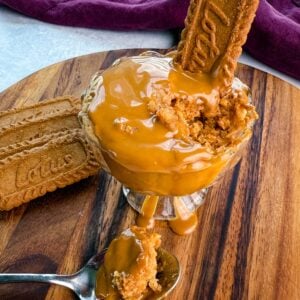 Glass dish of Biscoff mug cake topped with melted Biscoff spread and a Lotus cookie, with a spoonful of cake lifted up to show the texture.