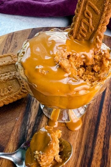 Glass dish of Biscoff mug cake topped with melted Biscoff spread and a Lotus cookie, with a spoonful of cake lifted up to show the texture.