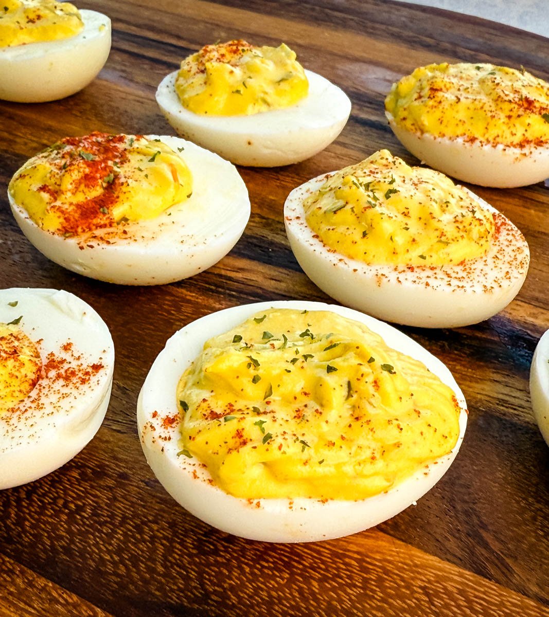 Deviled eggs on a wooden board with paprika and parsley garnish, close-up of creamy filling texture.