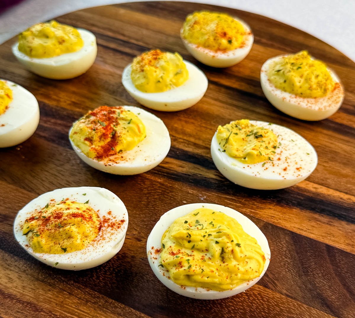 Overhead view of several deviled eggs arranged on a wooden platter, sprinkled with paprika and herbs.