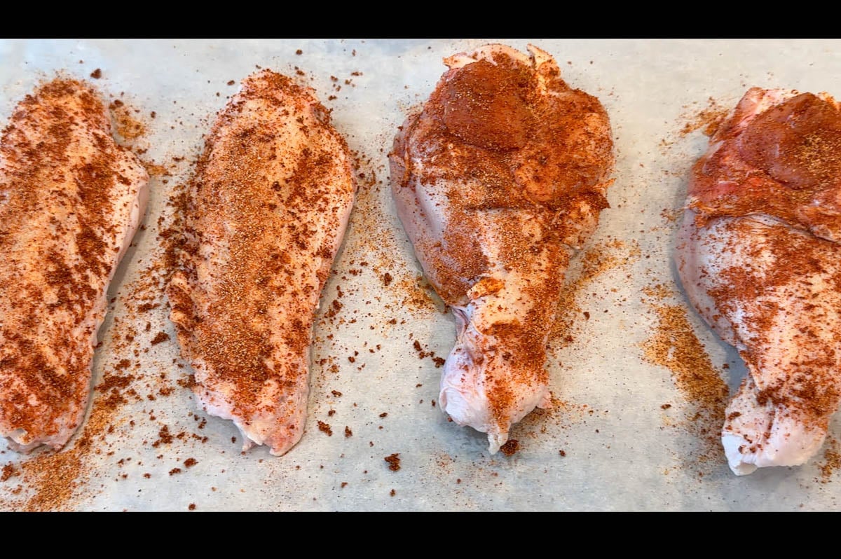Four raw turkey wings arranged on parchment paper, heavily seasoned with a reddish-brown spice blend.