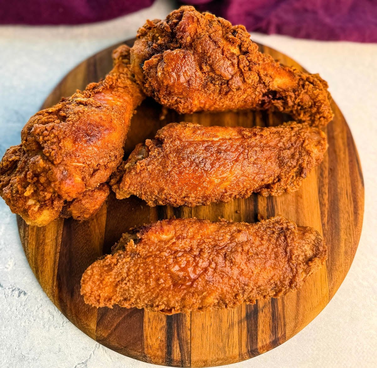 Four crispy fried turkey wings arranged on a wooden serving board, showcasing their crunchy, golden coating.