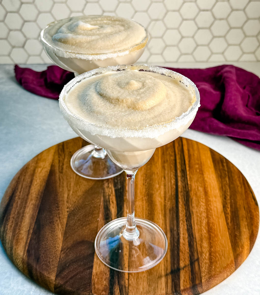 Two espresso martinis with icy, creamy texture in sugar-rimmed glasses, displayed on a round wooden board.