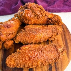 Close-up of golden brown fried turkey wings stacked on a round wooden board, with a deep purple cloth in the background.