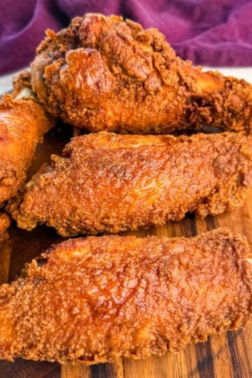 Close-up of golden brown fried turkey wings stacked on a round wooden board, with a deep purple cloth in the background.