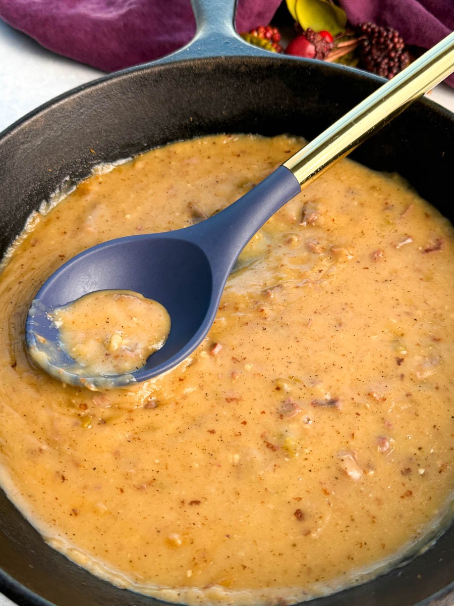 Cast iron skillet filled with thick turkey giblet gravy, with a blue and gold spoon lifting a scoop of the chunky, seasoned gravy.