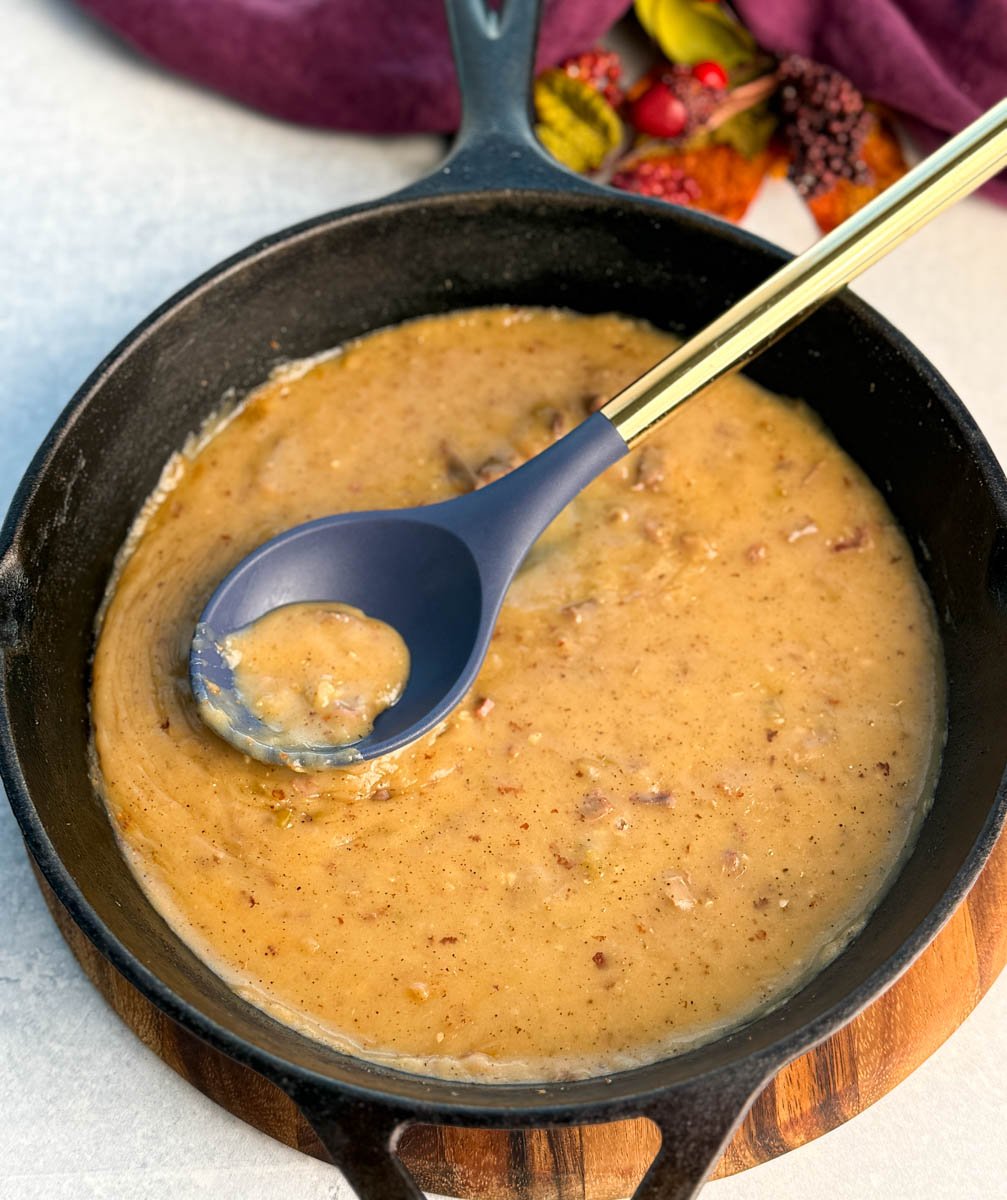 Top view of a skillet of smooth and chunky turkey giblet gravy, with a blue spoon resting inside.
