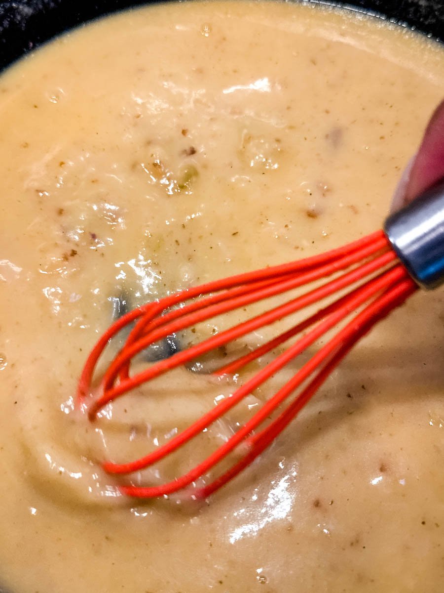 Giblet gravy being whisked smooth in a skillet with a bright red whisk.