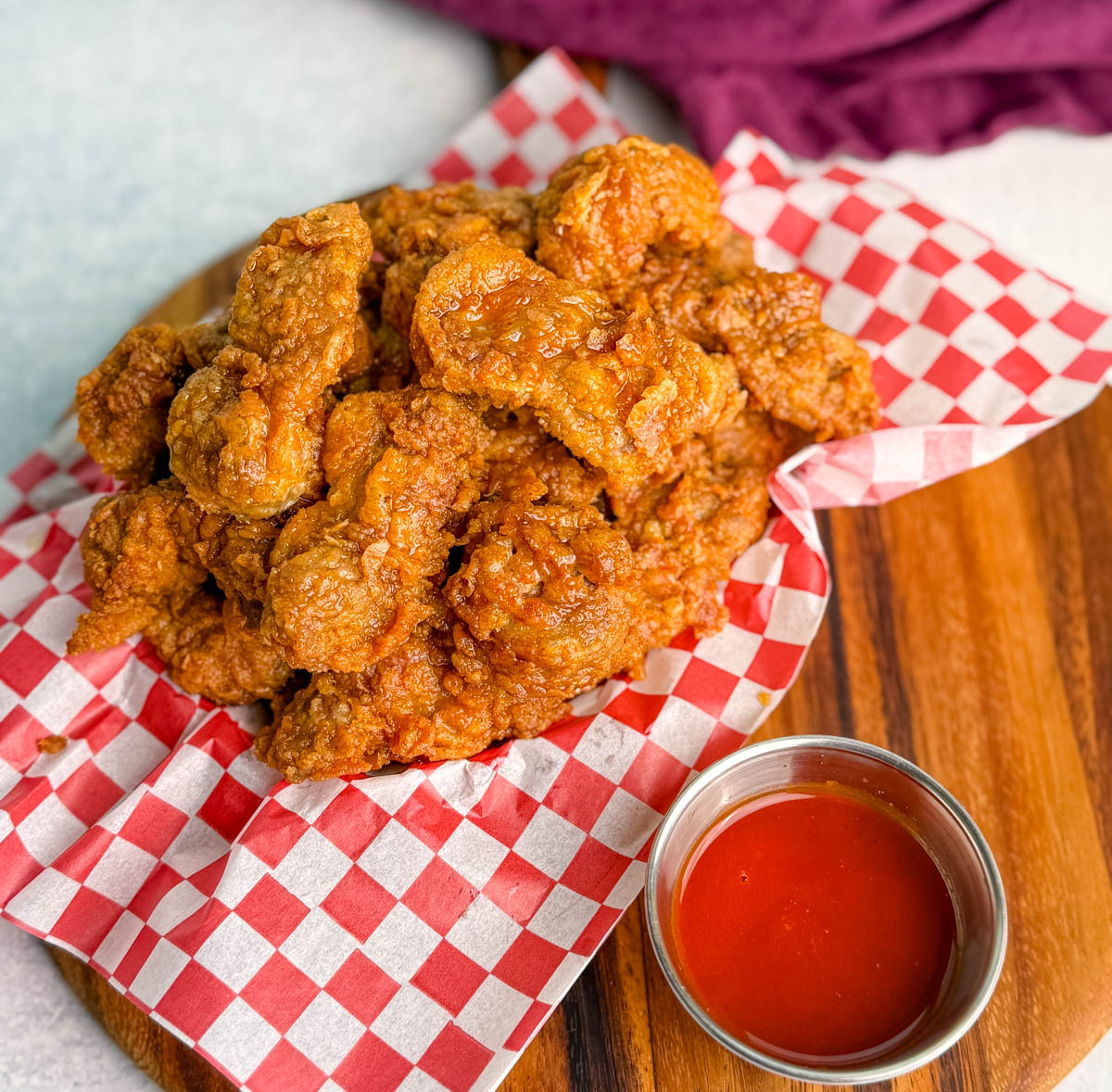 Basket of fried chicken gizzards on red and white checkered paper, served with a small cup of red dipping sauce.