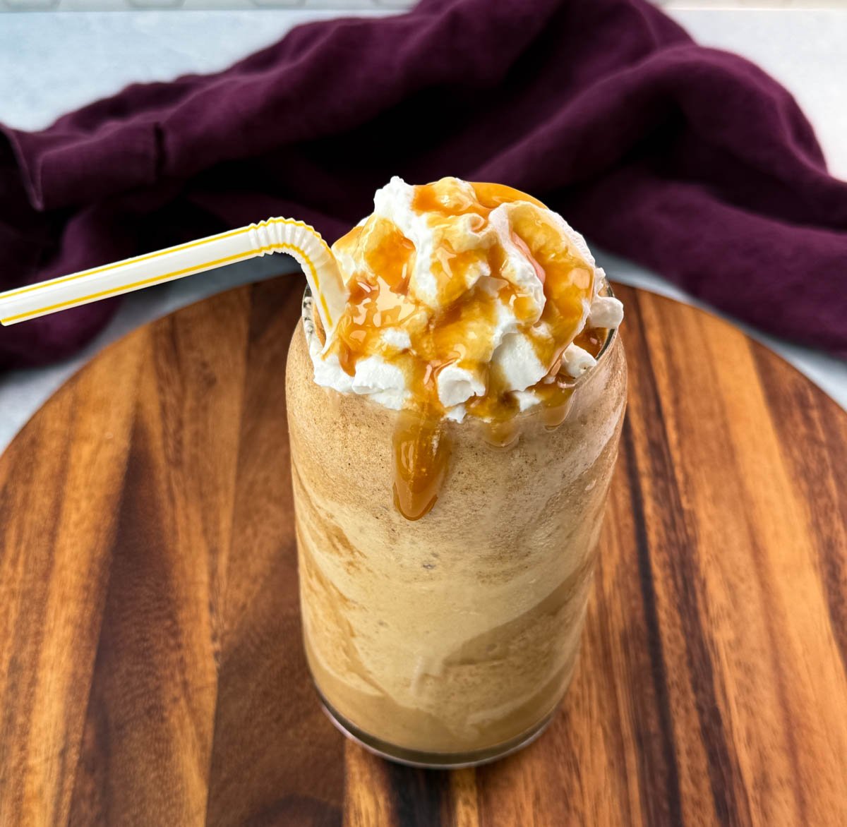 A tall glass of frappe topped with whipped cream and caramel drizzle, served with a straw.