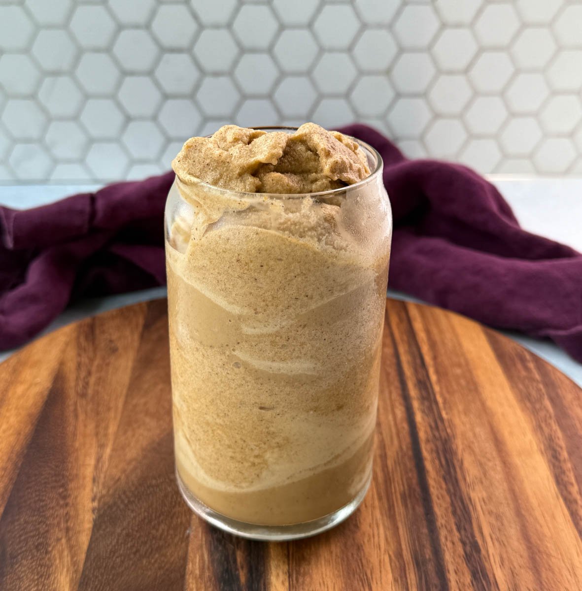 A tall glass filled with a thick pumpkin spice frappe with a swirled texture.