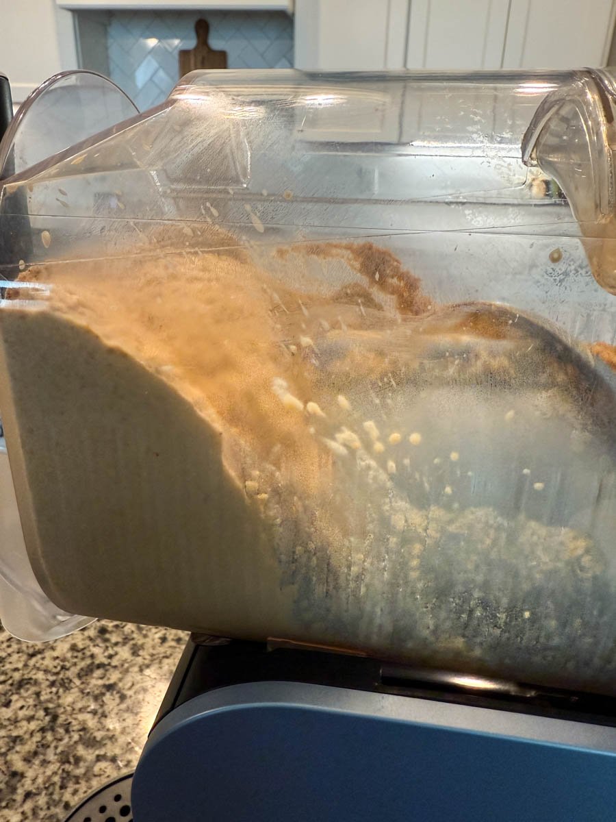 Thick pumpkin spice coffee frappe blending inside the clear container of a Ninja Slushi machine.