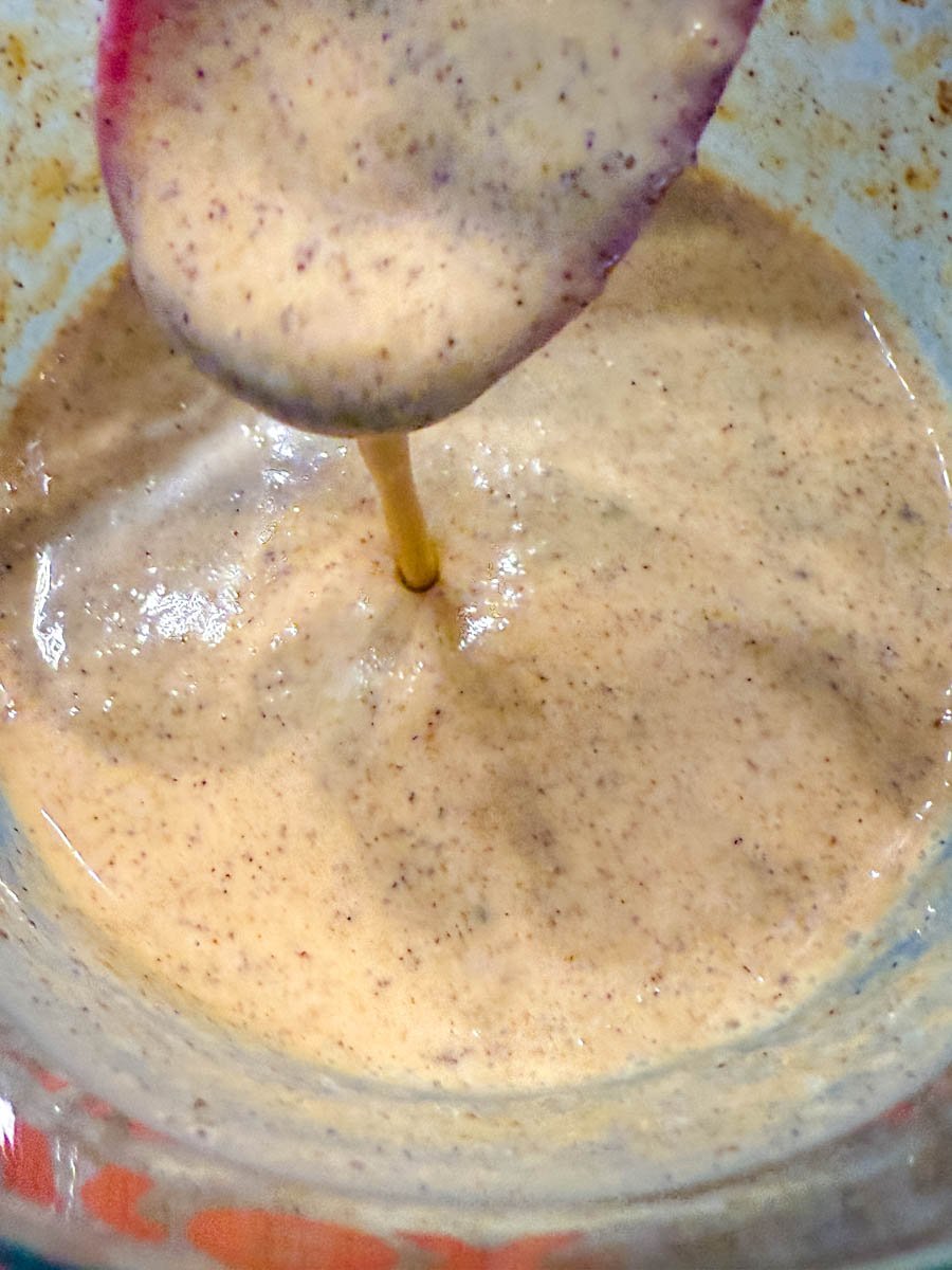A close-up of a frothy, spiced pumpkin mixture being stirred with a spoon.