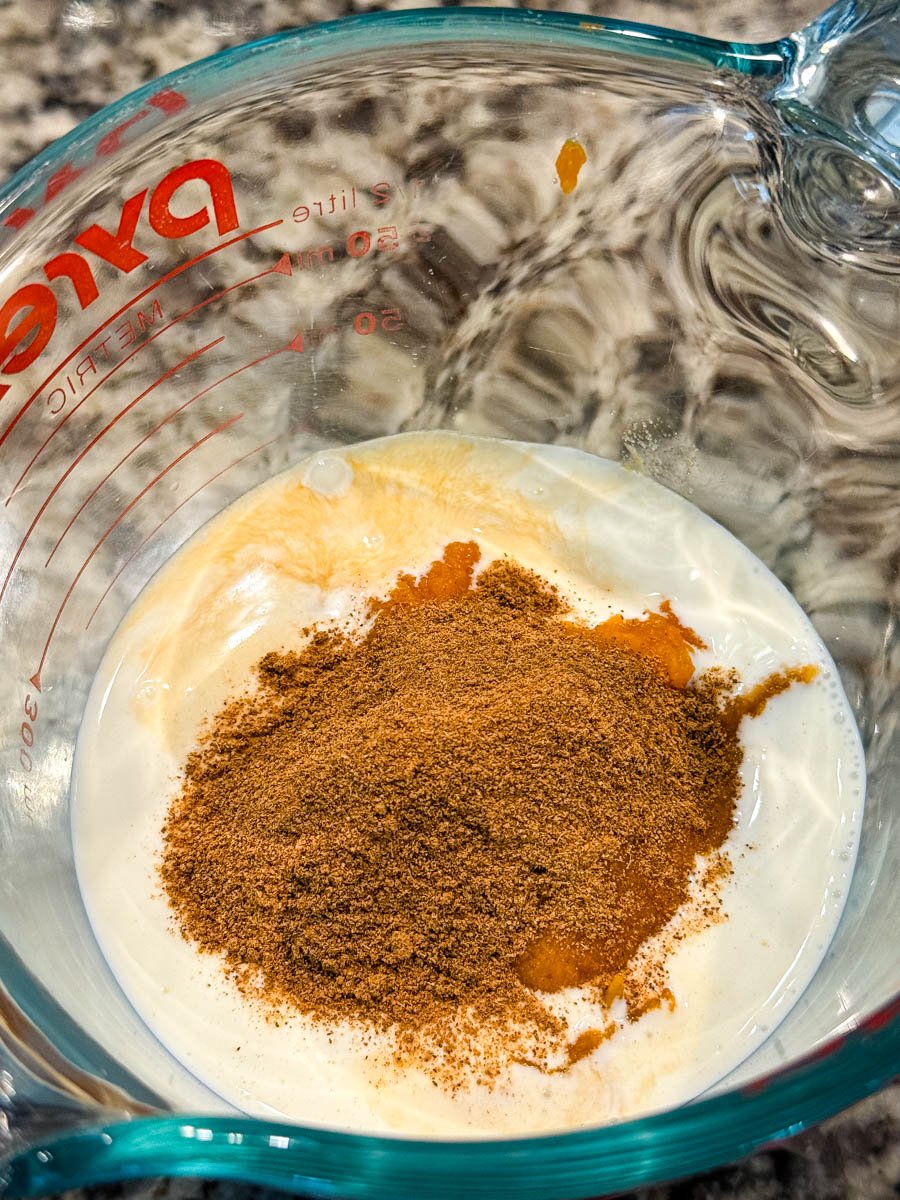 Milk, pumpkin purée, vanilla extract, and pumpkin pie spice combined in a glass measuring cup.
