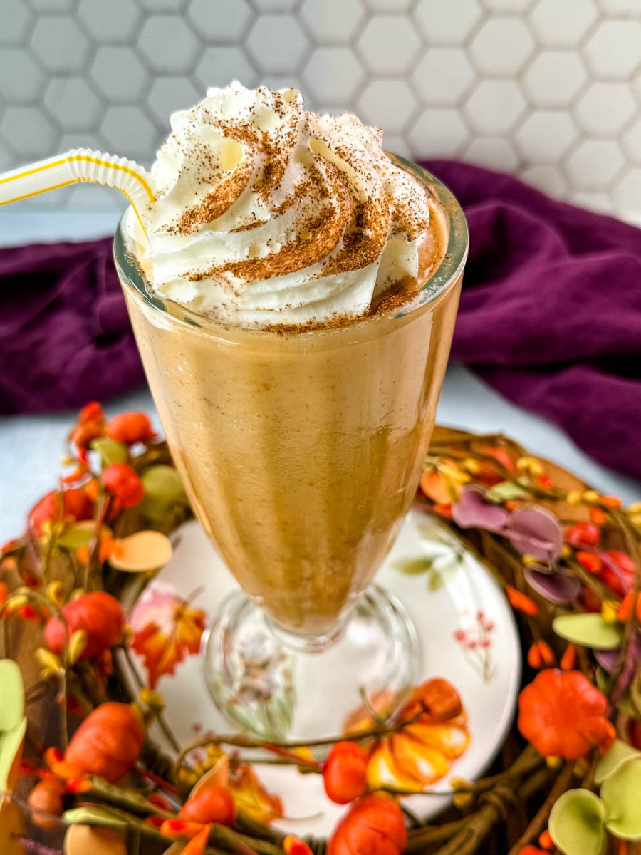 Close-up view of the milkshake glass with whipped cream swirled on top and dusted with pumpkin spice.