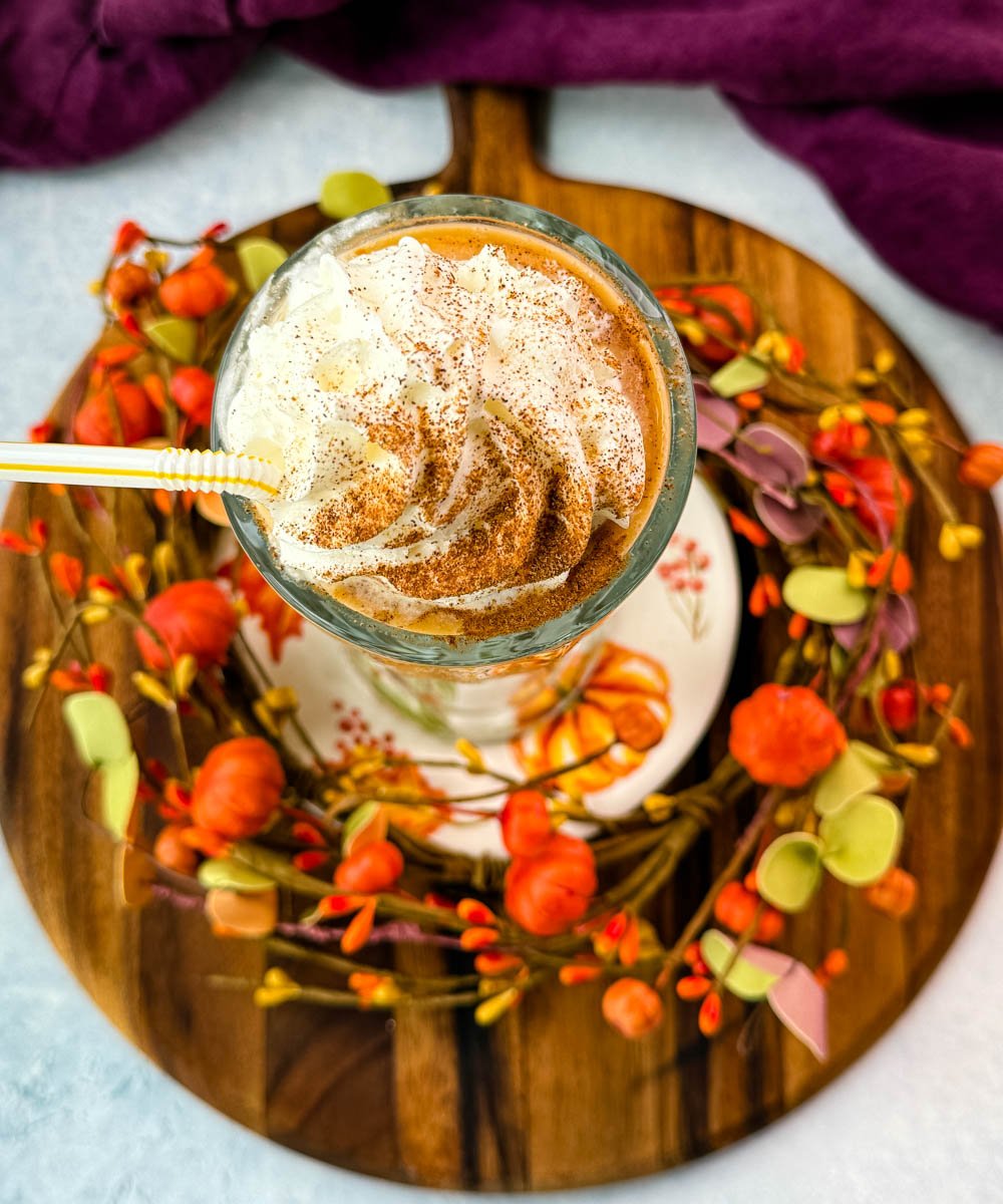 Top-down view of the whipped cream swirl on the pumpkin spice milkshake, sprinkled with cinnamon and served with a striped straw.