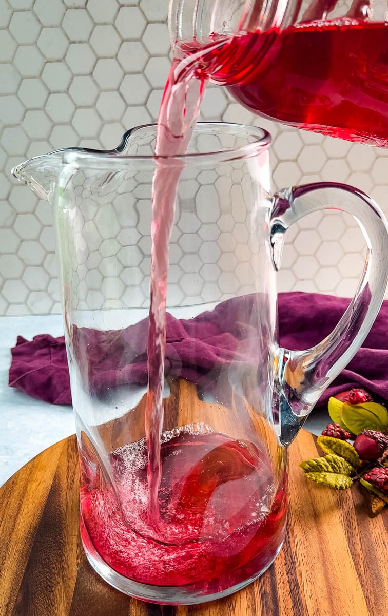 Cranberry juice being poured into an empty pitcher, beginning the Christmas punch base.