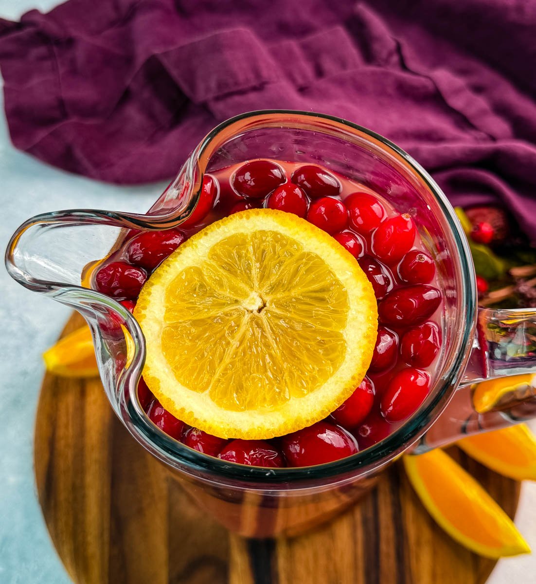 Close-up overhead of a pitcher showing cranberries and a large orange slice floating on the surface of the punch.