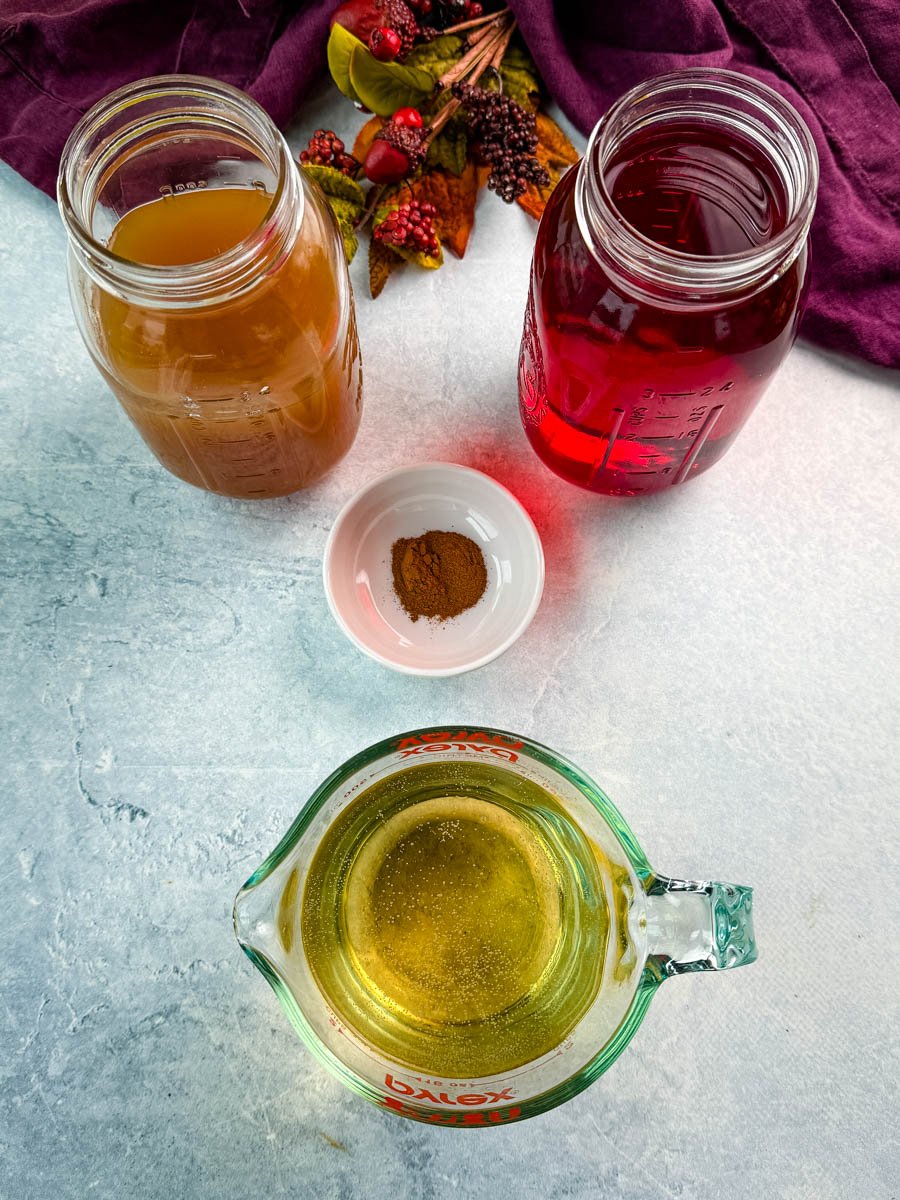Overhead shot of ingredients for Thanksgiving punch including apple cider, cranberry juice, ginger ale, and a small dish of ground cinnamon.