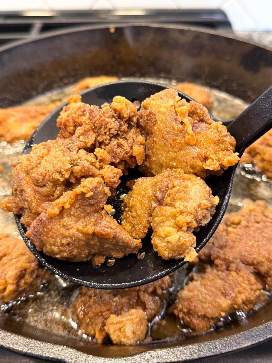 fried chicken livers in a slotted spoon over a pan of oil frying chicken livers