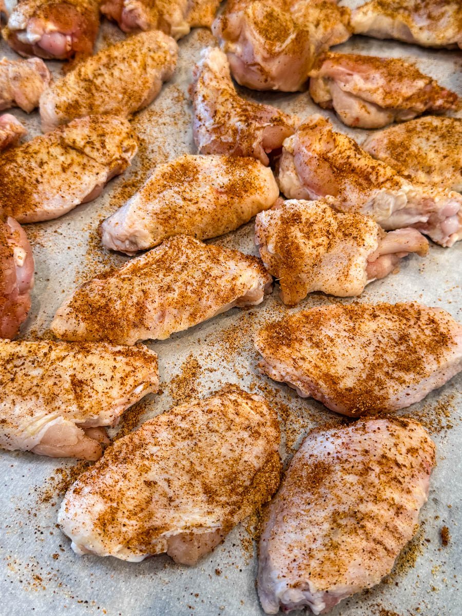 Raw chicken wings laid out on parchment paper, coated generously with seasoning.