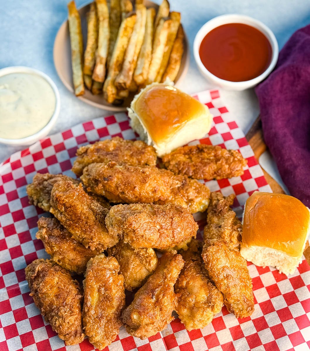 Overhead shot of crispy fried chicken wings on checkered paper, served with dinner rolls, fries, ranch, and buffalo dipping sauce.