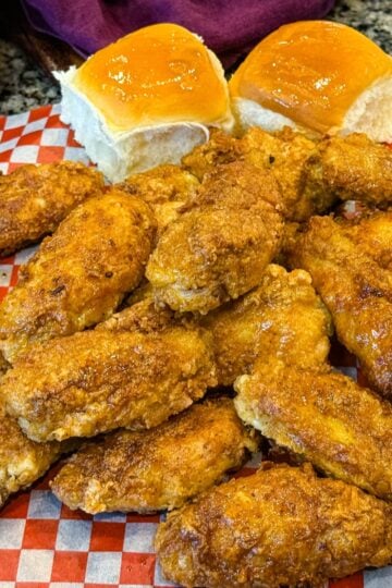 Overhead shot of crispy fried chicken wings on checkered paper, served with dinner rolls, fries, ranch, and buffalo dipping sauce.