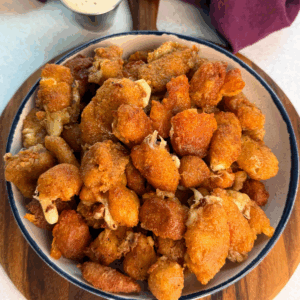 Overhead view of a large bowl filled with crispy fried cheese curds, showing crunchy coating and bits of melty cheese peeking through.
