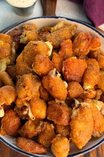 Overhead view of a large bowl filled with crispy fried cheese curds, showing crunchy coating and bits of melty cheese peeking through.