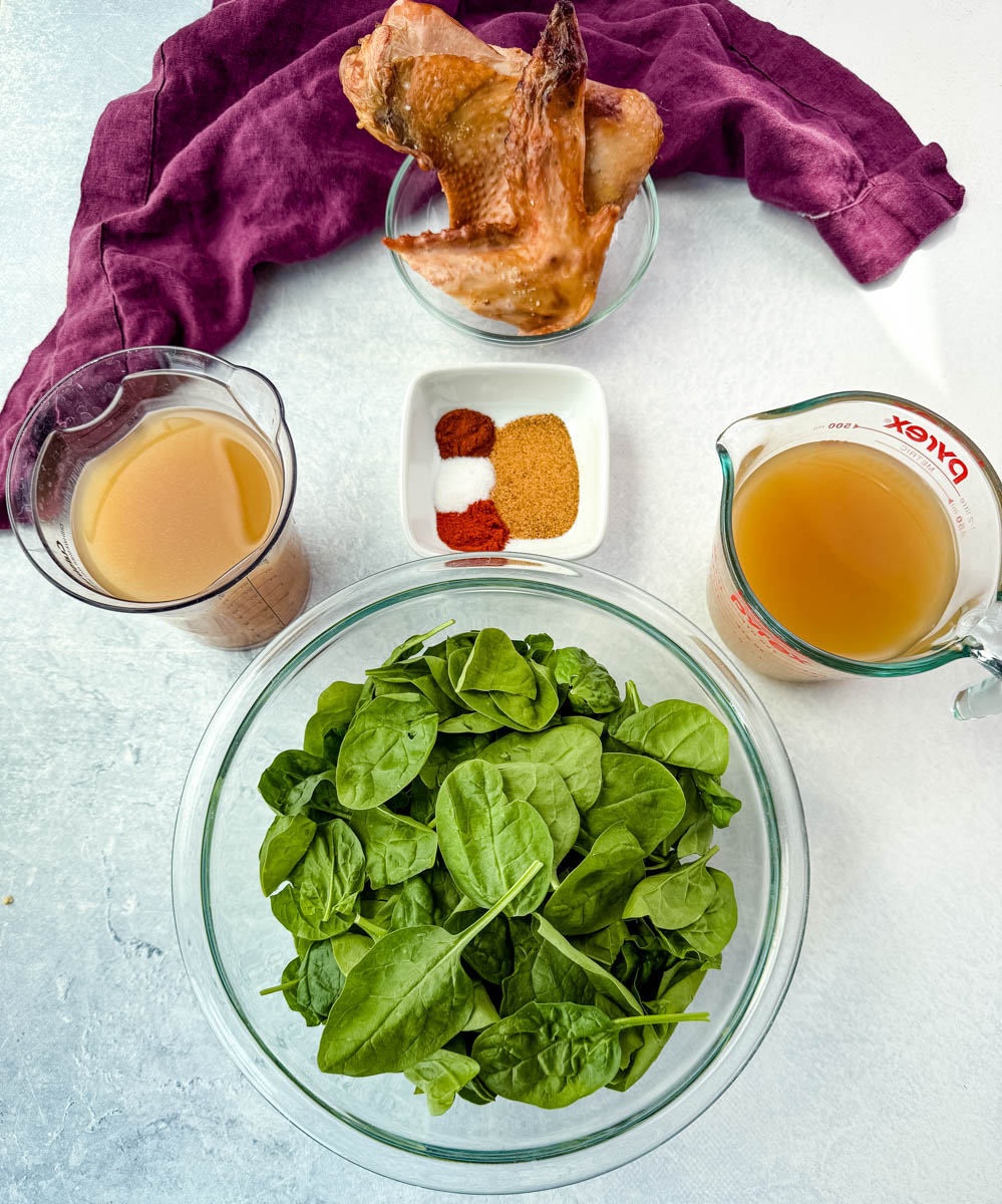 Bowls of fresh spinach, smoked turkey wing, chicken broth, spices, and seasonings arranged on a counter.