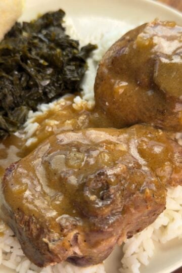 Plate of turkey chops smothered in brown gravy over rice, served with collard greens and a dinner roll.