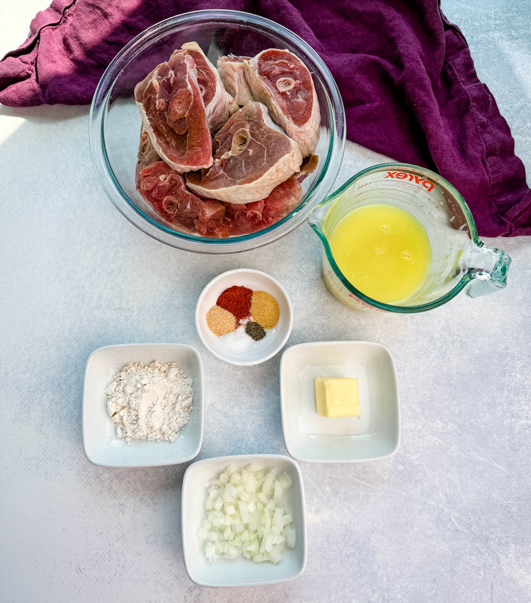Overhead shot of raw turkey chops and recipe ingredients laid out on a counter: chopped onions, butter, flour, spices, chicken broth, and a bowl of raw turkey chops.