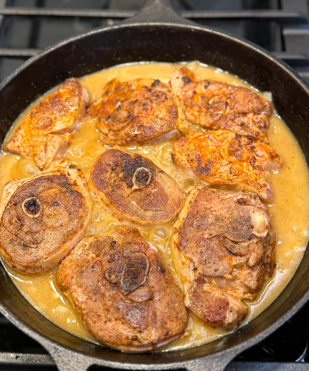 Cast iron skillet filled with browned turkey chops simmering in rich golden gravy.