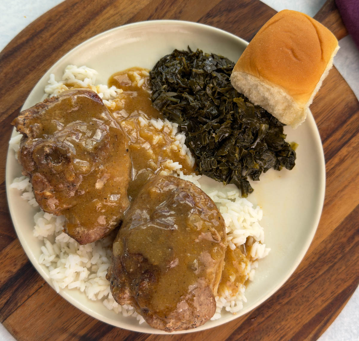 Overhead shot of a full plate—two turkey chops over rice with brown gravy, collard greens, and a roll on the side.