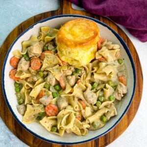 Close-up of a creamy one-pot chicken pot pie casserole with egg noodles, peas, and carrots served in a cast-iron skillet topped with golden biscuits.