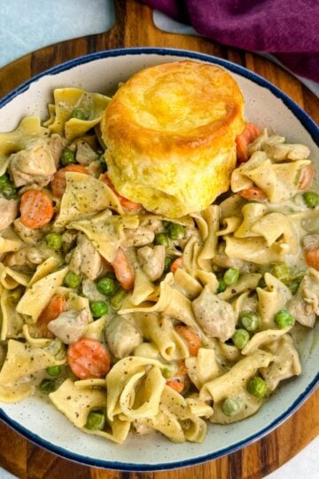 Close-up of a creamy one-pot chicken pot pie casserole with egg noodles, peas, and carrots served in a cast-iron skillet topped with golden biscuits.