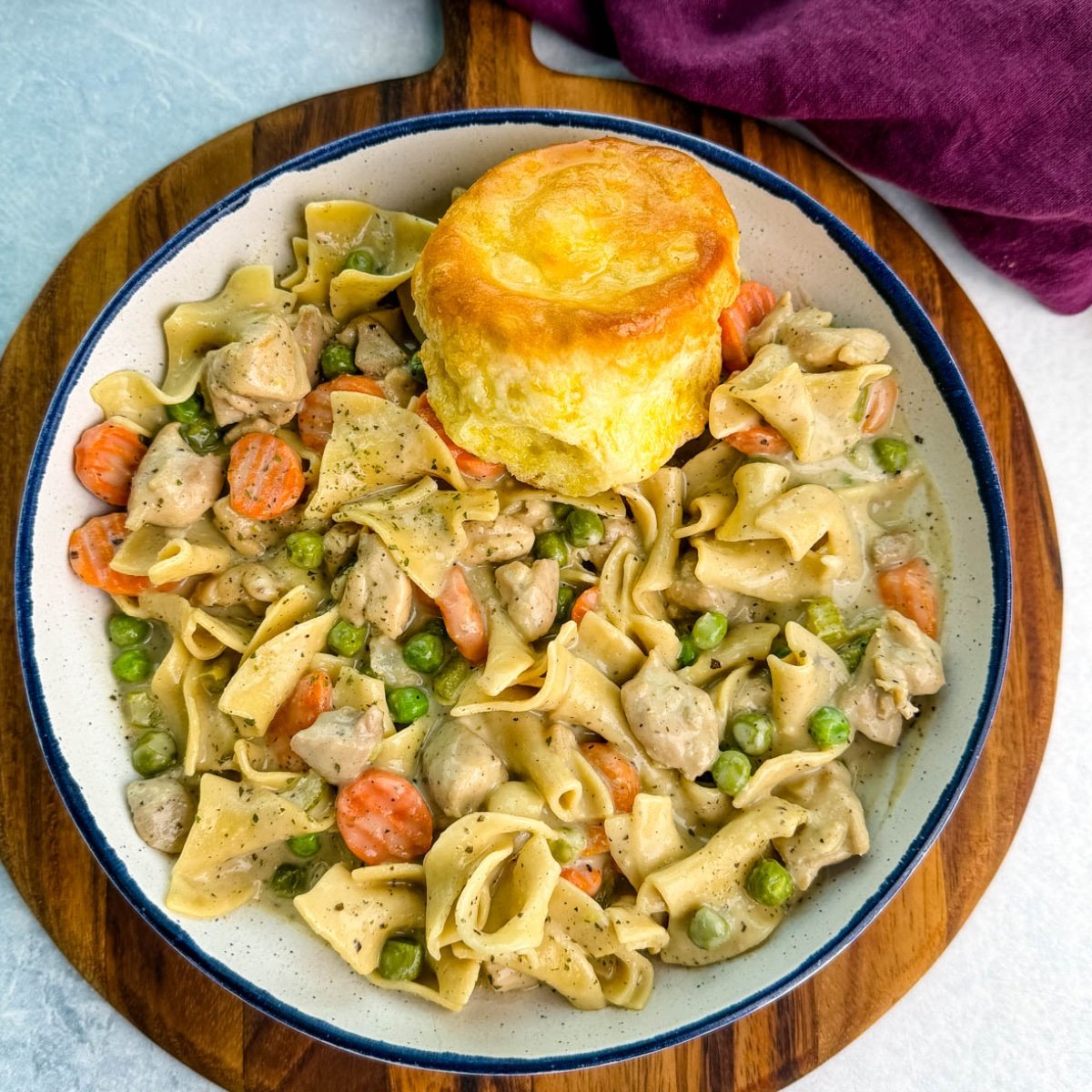 Close-up of a creamy one-pot chicken pot pie casserole with egg noodles, peas, and carrots served in a cast-iron skillet topped with golden biscuits.
