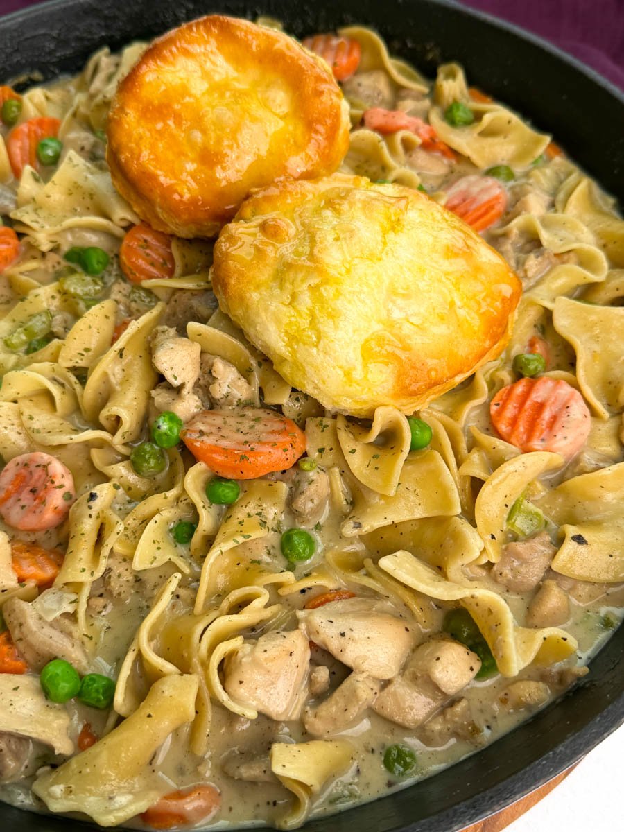 Close-up of creamy chicken pot pie casserole showing buttery noodles, seasoned chicken, peas, and carrots in a cast-iron skillet.