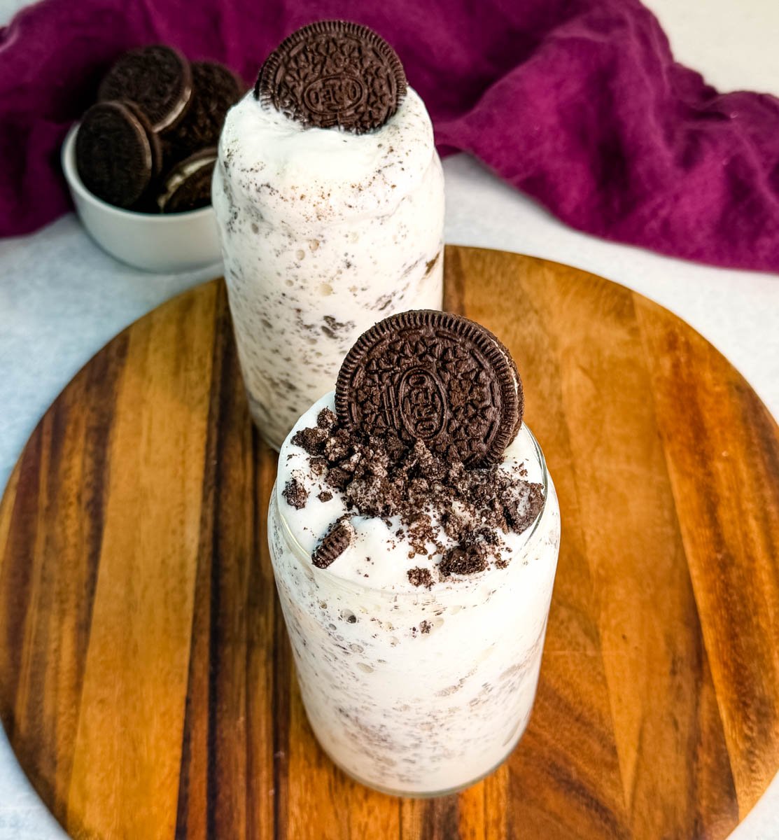 Overhead view of two Oreo Ninja Slushi McFlurries on a wooden board, each topped with crushed Oreos and a whole cookie.