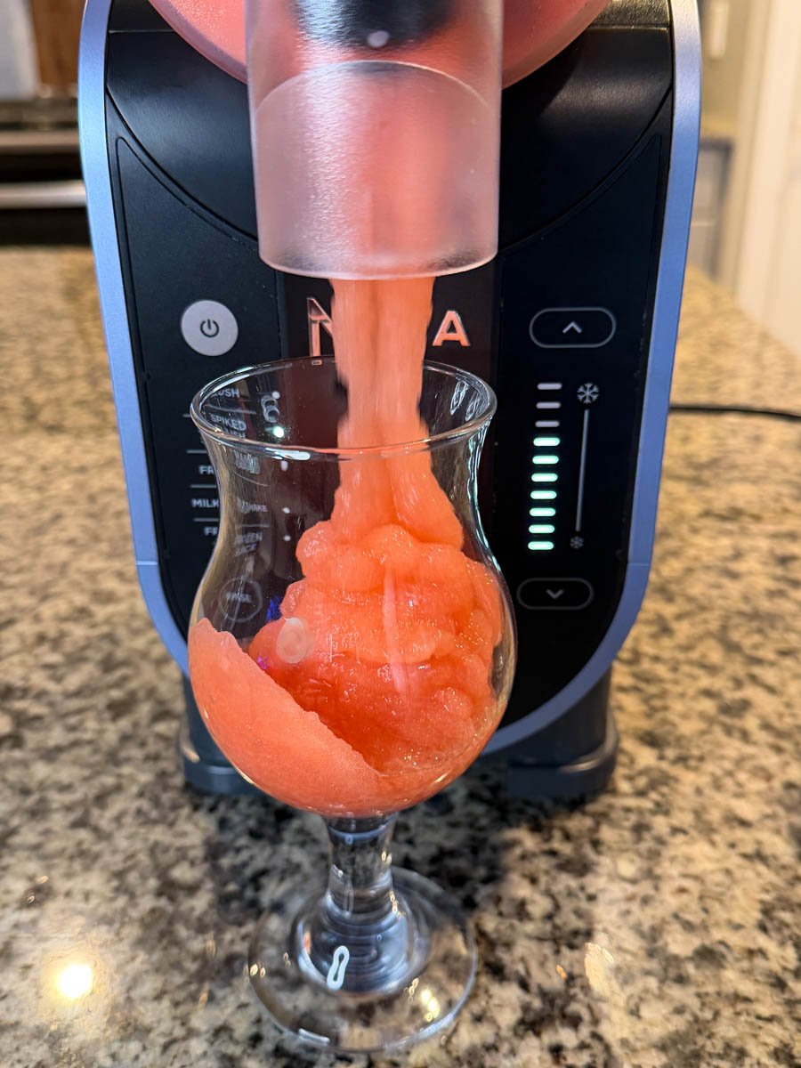 Dispensing the finished frozen rum punch from the Ninja Slushi machine into a glass.