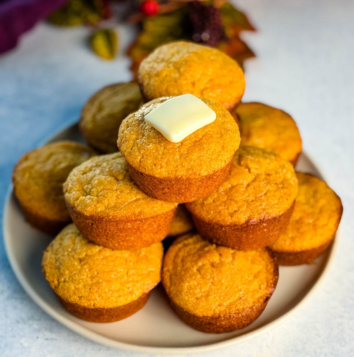 A full plate stacked with golden Jiffy sweet potato cornbread muffins, featuring a pat of butter melting on the top muffin.