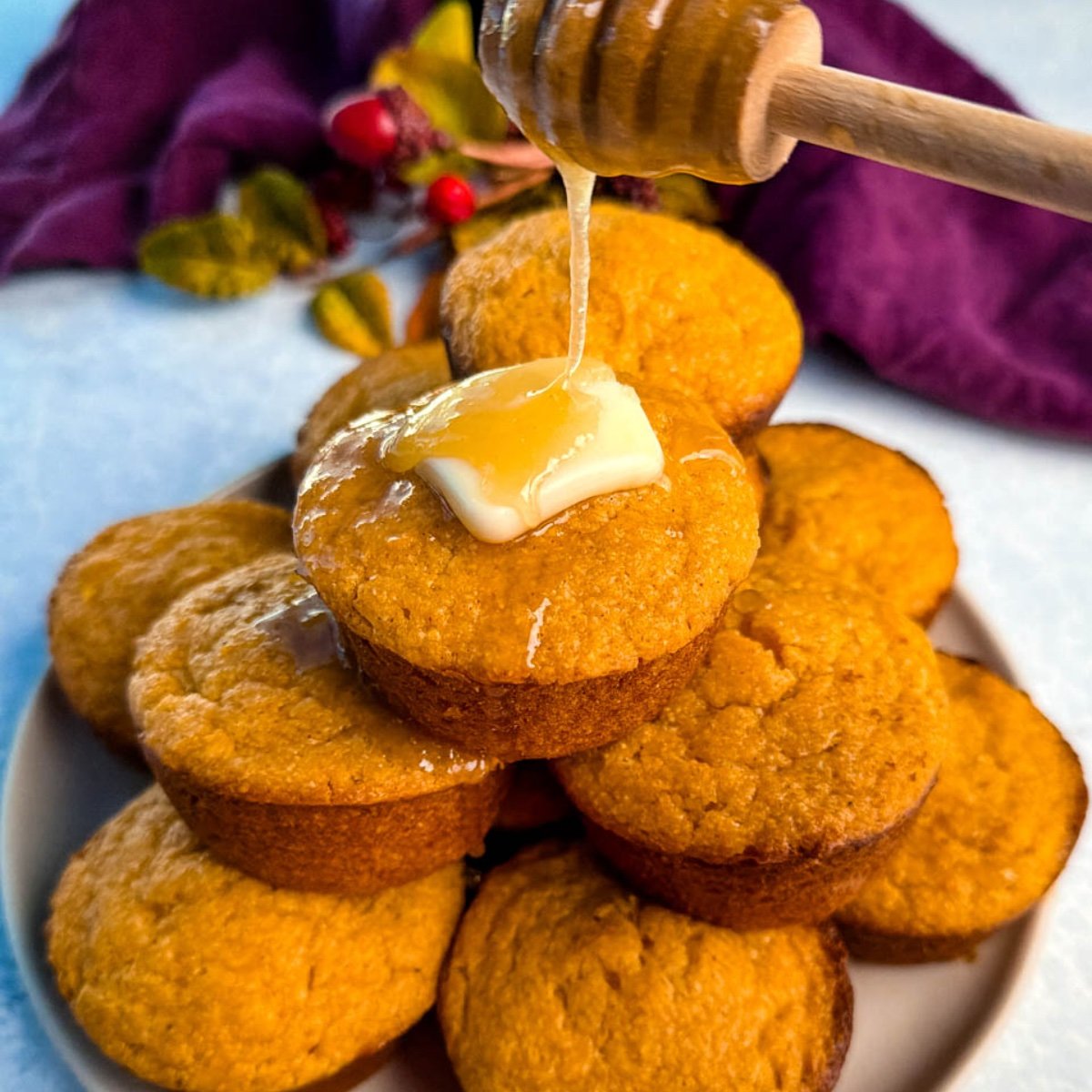 A stack of golden-brown Jiffy sweet potato cornbread muffins on a plate, topped with melting butter and drizzled with honey for a glossy, irresistible finish.